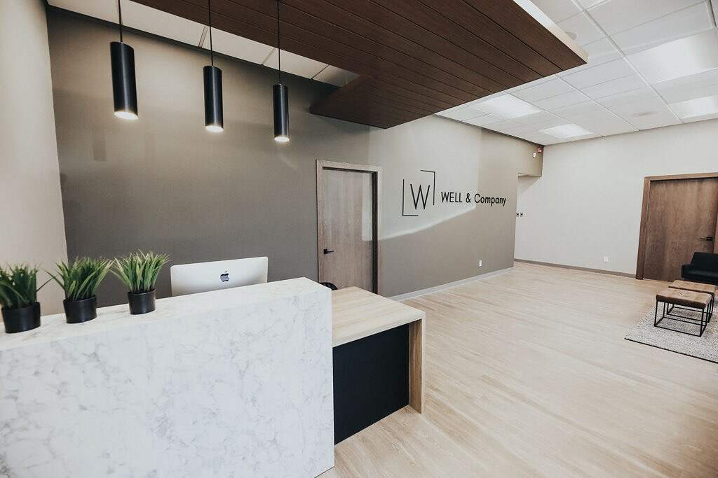 Modern office reception area featuring a sleek marble counter, minimalist décor, and pendant lighting by WELL & Company.