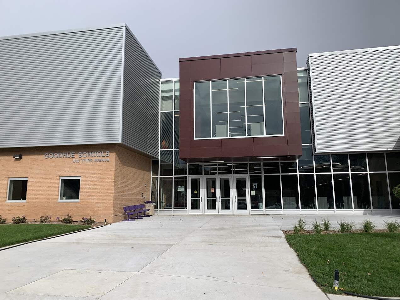 Modern Goodhue School building facade with a glass entrance and metallic exterior under overcast skies.