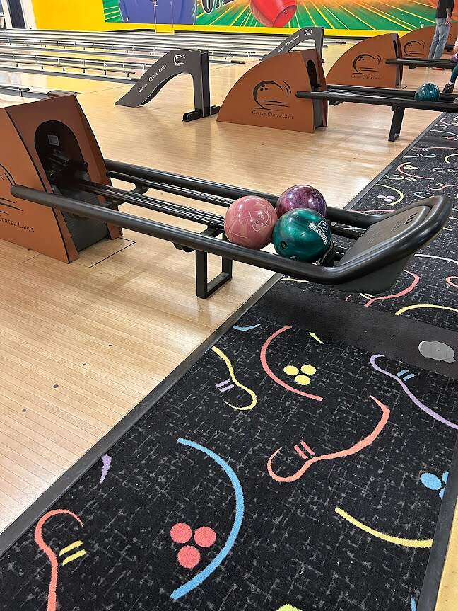 Colorful bowling balls ready for action on a busy alley with vibrant carpeting, showcasing the anticipation and excitement of a fun game ahead on the lanes.