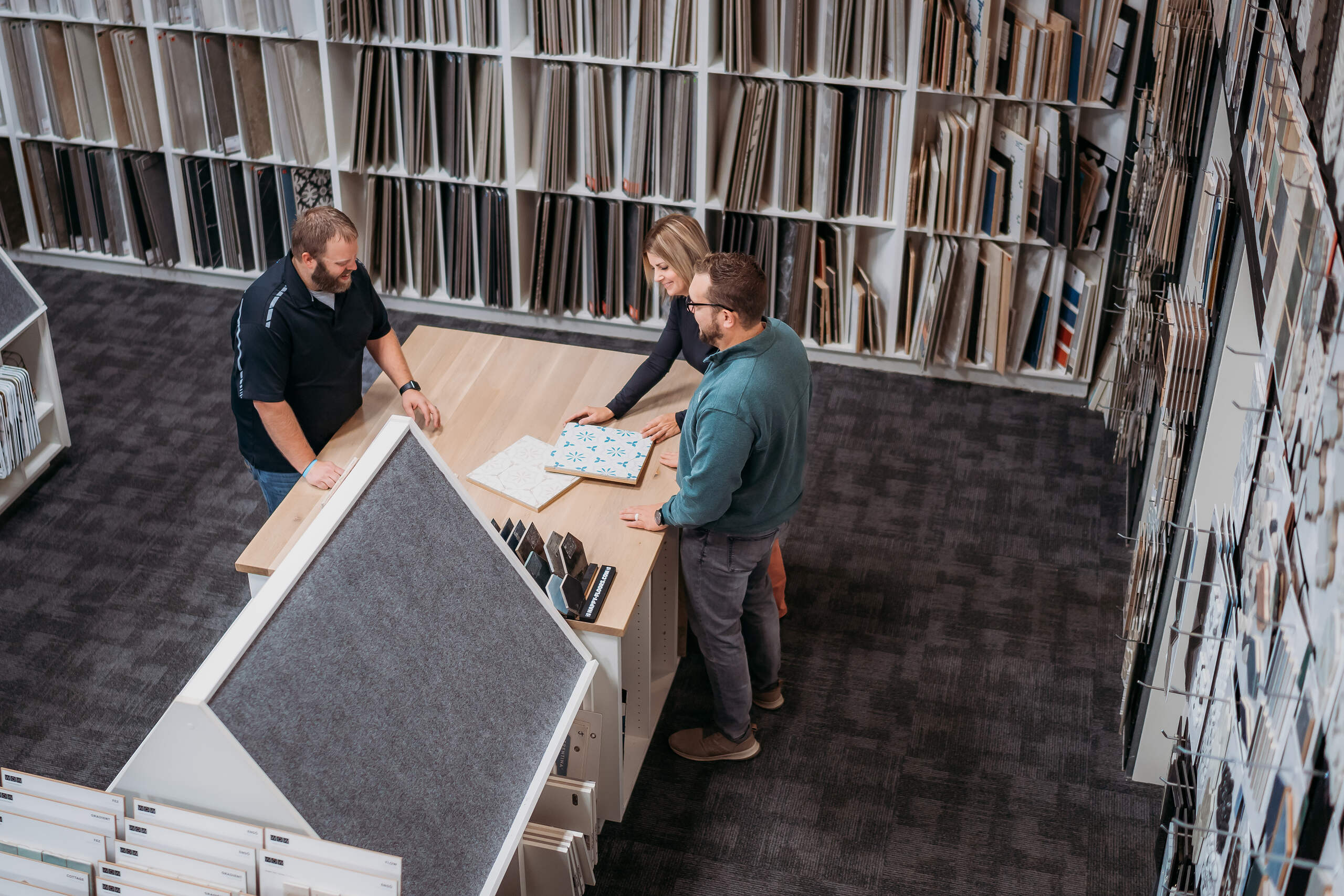 Three professionals collaborating over a map spread out on a table in a modern office environment, surrounded by shelves of documents and contact samples.