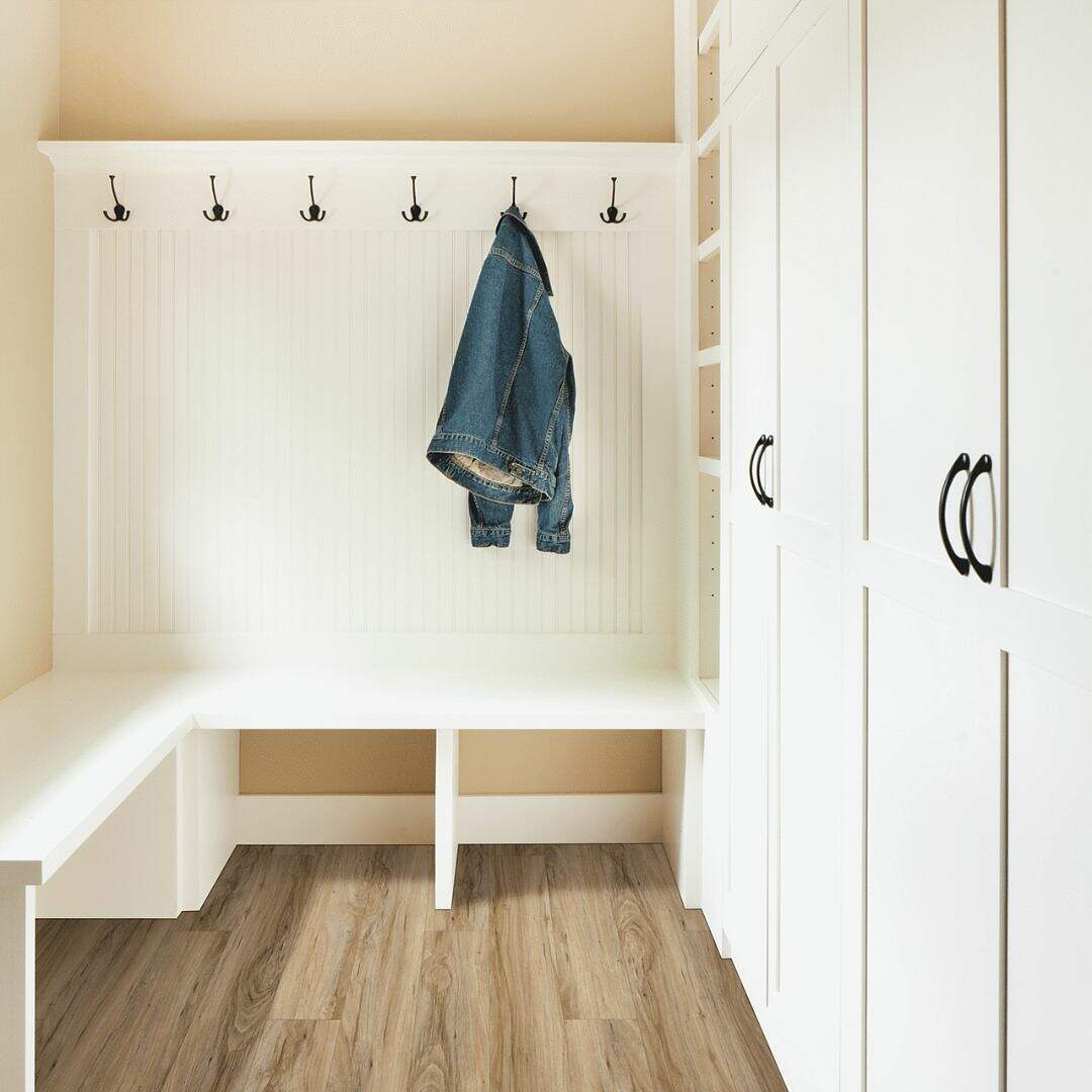 A clean and bright mudroom featuring white built-in cabinetry and a Seaside Sparrow Oak bench with a pair of jeans hanging on a hook against a neutral wall.