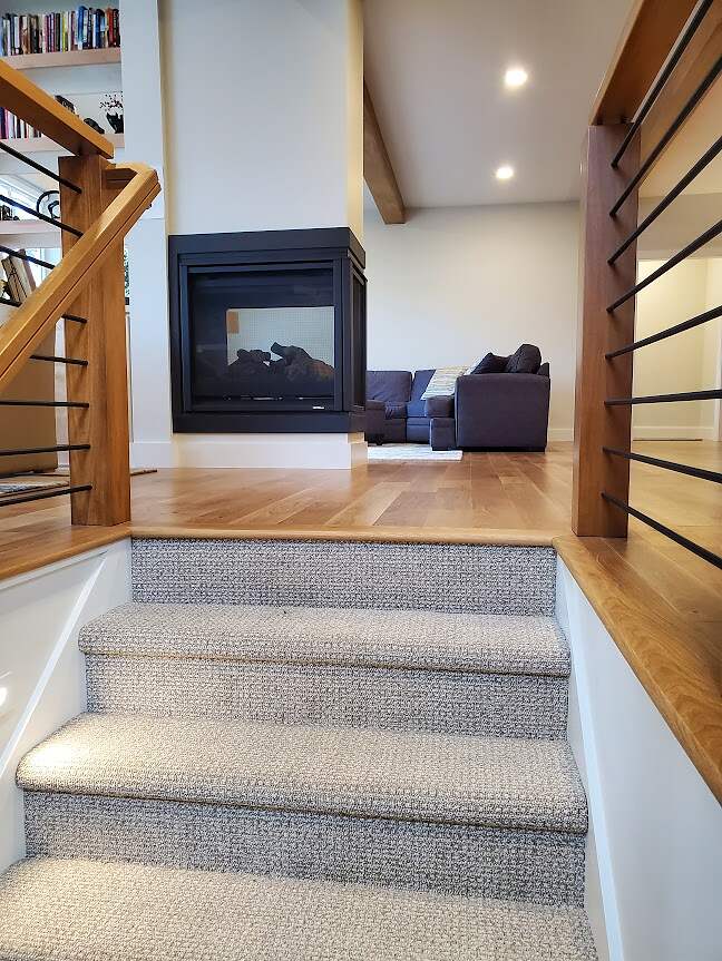 A modern home interior showcasing a staircase design with carpeted steps, wooden handrails, and metal balusters, leading up to a cozy landing with a fireplace and comfortable seating area.