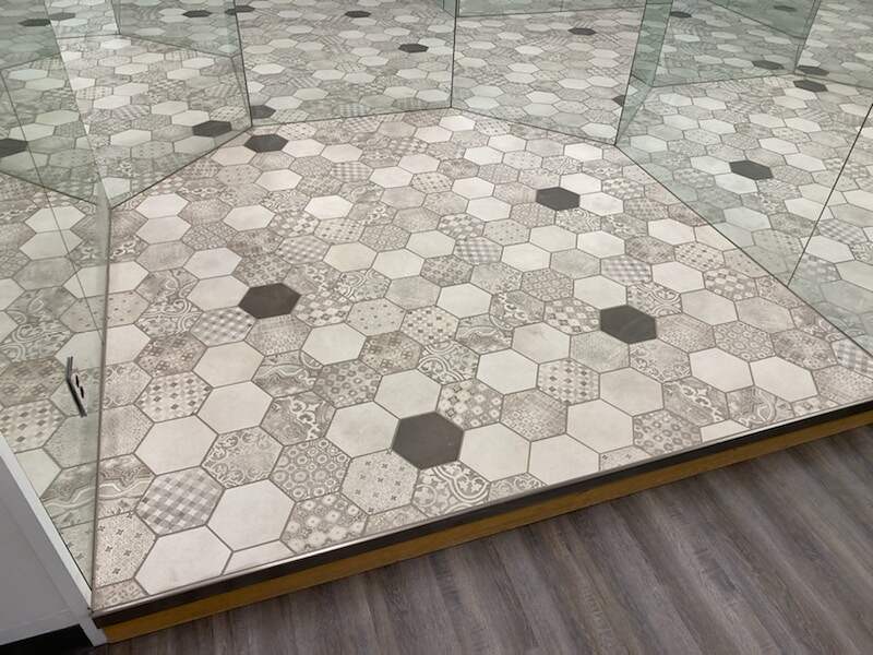 A modern glass display case on a decorative hexagonal-patterned tile floor in a retail space.