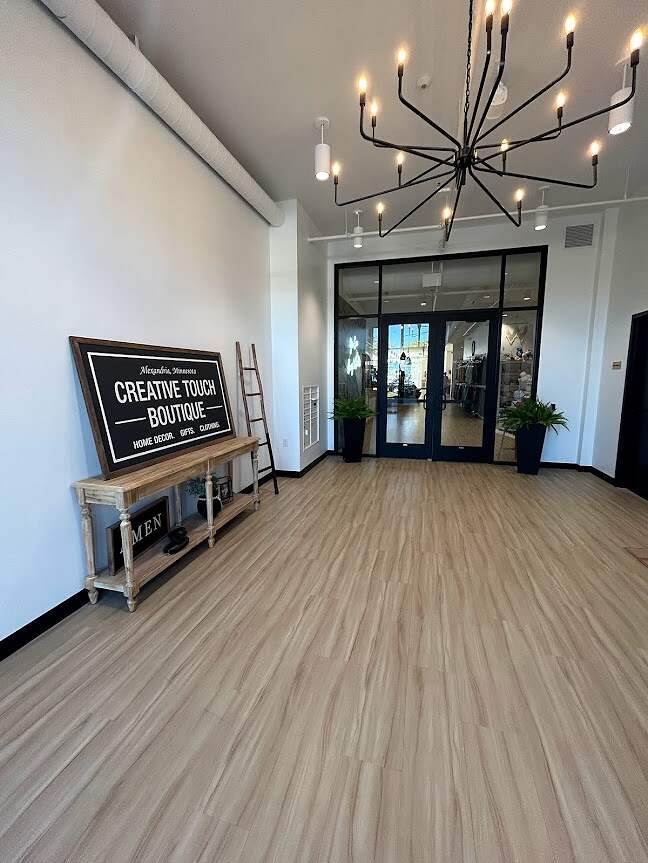 Elegant entrance foyer with a modern chandelier, wood-like flooring, and a welcoming boutique sign, exuding a Creative Touch.