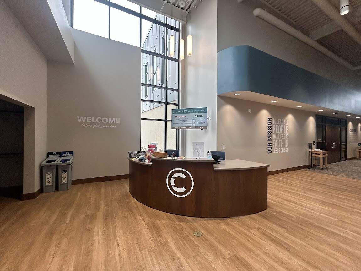 A modern lobby area of Calvary Lutheran Church with a welcoming reception desk, high ceilings, and informational screens about the Lutheran faith, ready to greet visitors with a friendly atmosphere.
