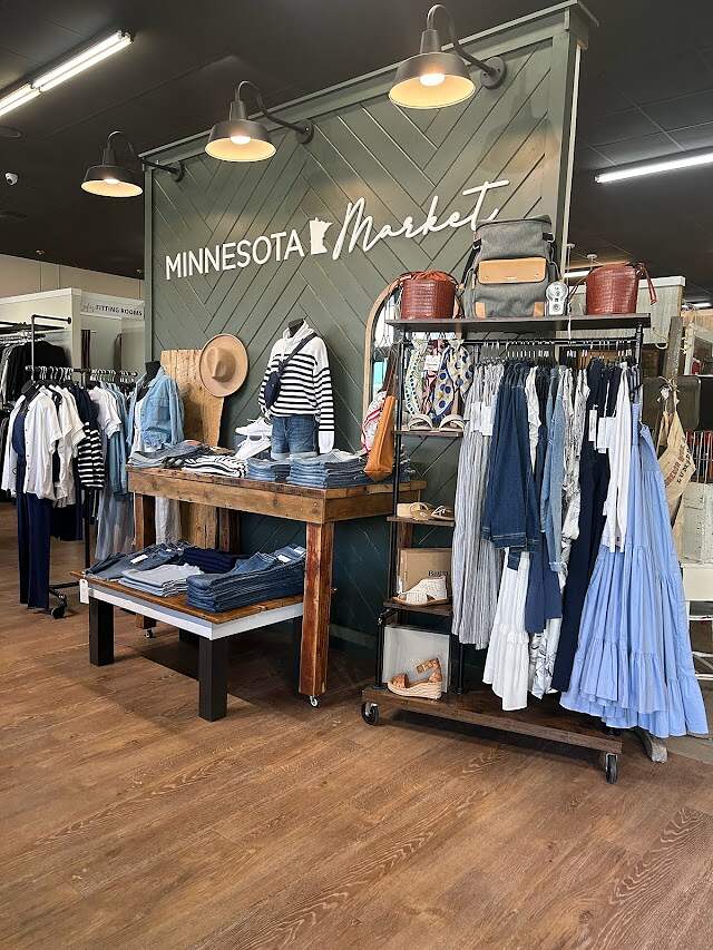 A boutique clothing store interior, featuring an assortment of stylish garments and accessories tastefully displayed on wooden racks and tables, with a sign reading 
