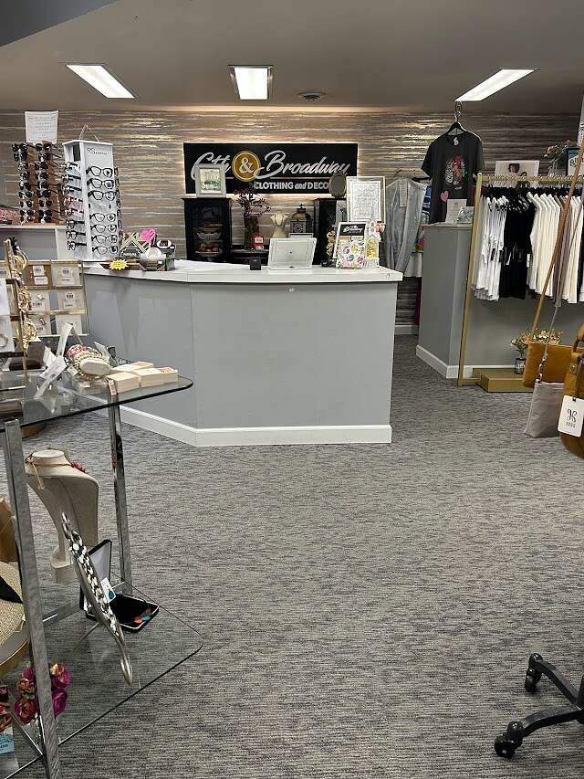 A quaint boutique shop interior with a variety of items on display, featuring a front counter labeled "6th & Broadway Clothing and Décor," ready to welcome customers.